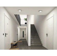 Moderner, heller Flur mit weißen Türen, einer grauen Betontreppe und quadratischen LED-Deckenleuchten.