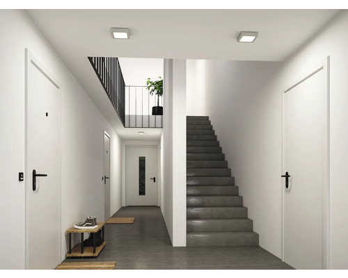 Moderner, heller Flur mit weißen Türen, einer grauen Betontreppe und quadratischen LED-Deckenleuchten.