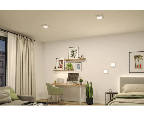 Moderner, hell gestalteter Wohnraum mit Schreibtisch und Bett, beleuchtet durch quadratische LED Einbauleuchten an der Decke und Wandleuchten.