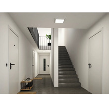 Moderner, heller Flur mit weißen Türen, einer dunklen Treppe und einer quadratischen LED-Deckenleuchte.