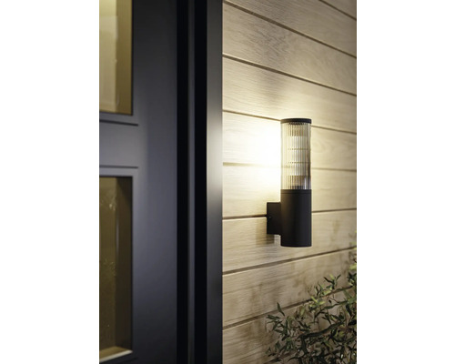 Moderne Außenwandleuchte mit schwarzem, zylindrischem Sockel und geripptem Glasaufsatz, montiert an einer Holzwand neben einer Tür.