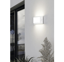 Moderne weiße LED-Außenwandleuchte in gewölbtem Design, montiert an einer Fassade neben einem Fenster, hell leuchtend.