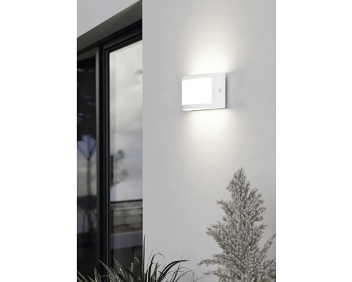 Moderne weiße LED-Außenwandleuchte in gewölbtem Design, montiert an einer Fassade neben einem Fenster, hell leuchtend.