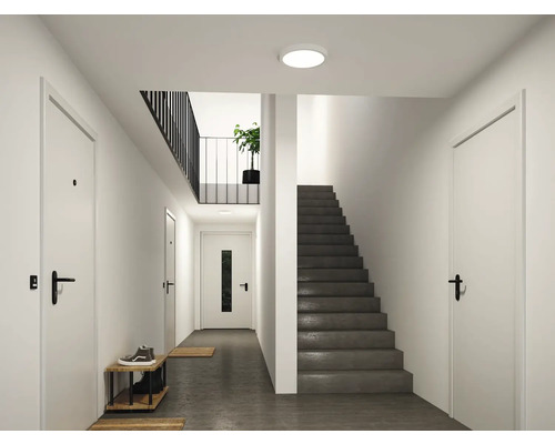 Moderner, heller Flur mit runder Deckenleuchte, grauer Treppe, weißen Türen und schwarzem Geländer.