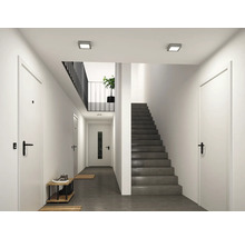 Moderner heller Flur mit weißen Innentüren, schwarzen Griffen, dunkelgrauer Treppe und quadratischen Deckenleuchten.