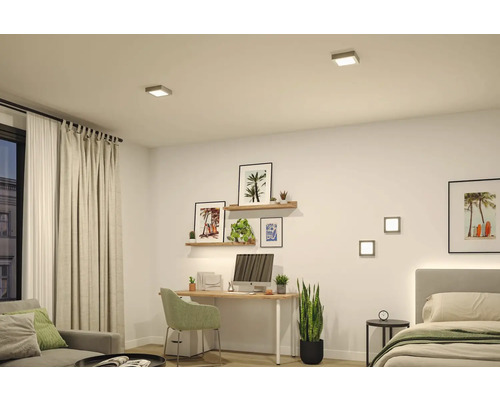 Heller moderner Raum mit quadratischen LED Decken- und Wandleuchten. Strukturierter Bereich mit Schreibtisch, Bett, Sitzmöbeln und Zimmerpflanzen.