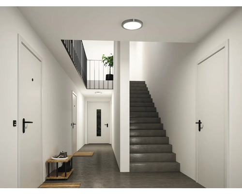 Moderner, heller Flur mit weißen Türen, einer dunklen Treppe und einer runden Deckenleuchte aus Metall.