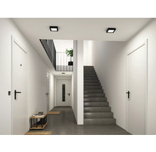 Heller, moderner Flur mit weißen Türen, schwarzen Türgriffen, einer grauen Betontreppe und quadratischen schwarzen Deckenleuchten.