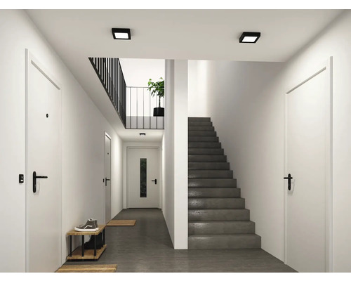 Heller, moderner Flur mit weißen Türen, schwarzen Türgriffen, einer grauen Betontreppe und quadratischen schwarzen Deckenleuchten.