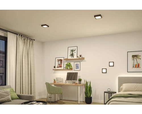 Moderner, heller Raum mit Arbeitsbereich, Bett und Sofa, beleuchtet durch quadratische schwarze LED-Decken- und Wandleuchten.