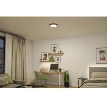 Moderne, helle Inneneinrichtung mit einer runden schwarzen LED-Deckenleuchte über einem Arbeitsplatz mit Schreibtisch, Sessel und einem Bett.