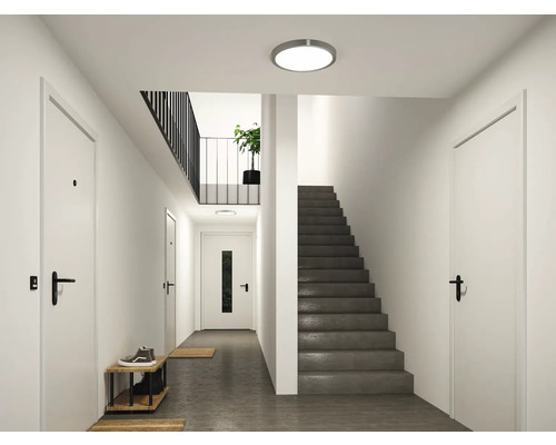 Moderner, heller Flur mit einer runden LED Deckenleuchte, weißen Türen und einer dunkelgrauen Treppe.