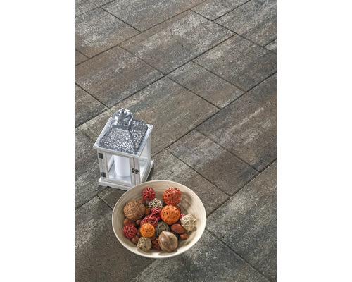 Rechteckige Pflastersteine aus Beton in schattierter Optik auf einer Terrasse, dekoriert mit einer Laterne und einer Schale.