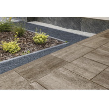 Großformatige Terrassenplatten aus Beton neben einer Gartenfläche mit dunklem Splitt, Rindenmulch und kleinen Sträuchern.