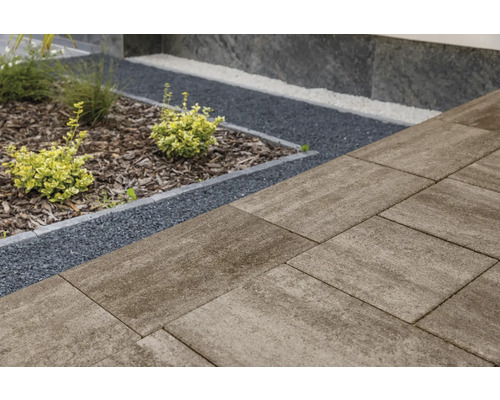 Großformatige Terrassenplatten aus Beton neben einer Gartenfläche mit dunklem Splitt, Rindenmulch und kleinen Sträuchern.