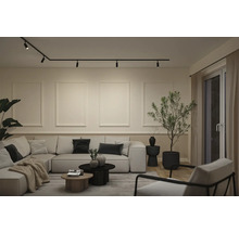 Modernes Wohnzimmer mit schwarzem Schienensystem an der Decke, großem hellem Ecksofa und minimalistischer Wandgestaltung.