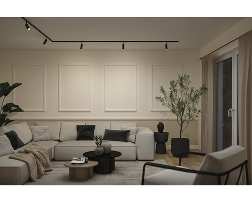 Modernes Wohnzimmer mit schwarzem Schienensystem an der Decke, großem hellem Ecksofa und minimalistischer Wandgestaltung.