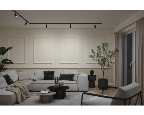 Modernes Wohnzimmer mit Schienensystem an der Decke, Wandleisten, großem Ecksofa, Couchtischen und einer Zimmerpflanze.