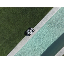Mähroboter an der Kante einer Rasenfläche neben einem Pool mit Steineinfassung in der Draufsicht.