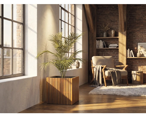 Quadratischer Pflanzkübel aus Holzlamellen mit einer Zimmerpflanze in einem hellen Wohnraum mit Backsteinwand und großen Fenstern.