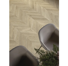 Laminatboden mit Chevron-Muster in Eichenoptik in einem modern eingerichteten Raum mit grauen Sesseln und Pflanzen.