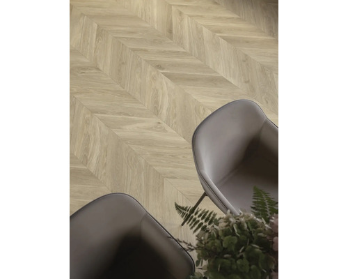 Laminatboden mit Chevron-Muster in Eichenoptik in einem modern eingerichteten Raum mit grauen Sesseln und Pflanzen.