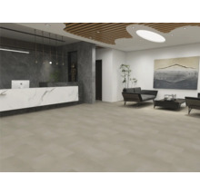 Modern gestalteter Empfangsbereich mit großflächigen, beigen Bodenfliesen, einer Marmor-Optik-Theke und einer Sitzecke mit dunklen Sofas.