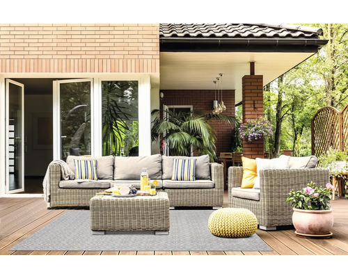 Hell gestaltete Terrasse mit Polyrattan-Sitzgruppe, gemustertem Outdoorteppich, gelbem Strick-Pouf und Pflanzen auf einem Holzdeck.