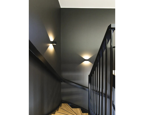 Moderne Treppe mit dunklen Wänden, Holzstufen und schwarzem Geländer. Zwei Wandleuchten mit Lichtstrahlen nach oben und unten setzen Akzente.