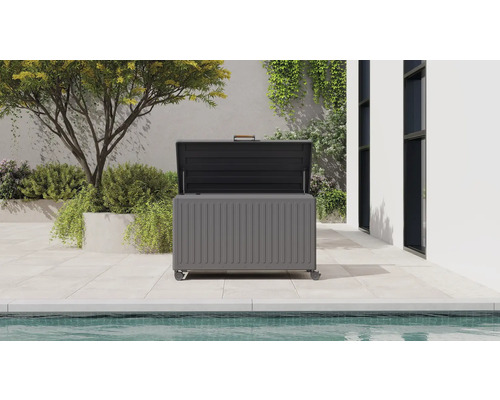 Moderne Gartenbox aus Metall mit offenem Deckel auf einer hellen Terrasse neben einem Pool.