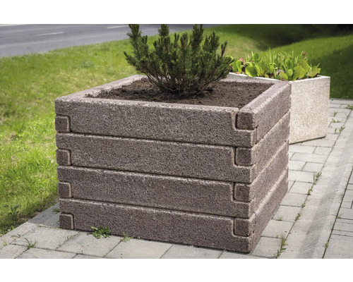 Quadratischer Pflanzkübel aus Beton mit strukturierter Steinoberfläche, gestapeltes Design, bepflanzt mit einem kleinen Nadelbaum auf einem Gehweg.