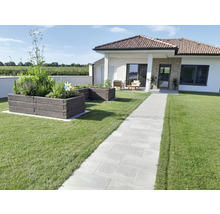 Moderner Garten mit gepflastertem Weg aus hellgrauen Platten, zwei Hochbeeten aus dunklen Modulsteinen und einem Bungalow im Hintergrund.