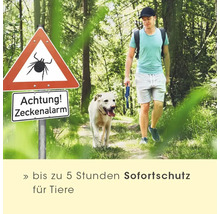 Mann und Hund spazieren im Wald neben einem Zecken-Warnschild, mit Hinweis auf bis zu fünf Stunden Sofortschutz für Tiere.