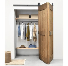 Zweiflügelige Schiebetür aus Holz im Scheunentor-Stil vor einem organisierten Kleiderschrank mit schwarzem Schienensystem.