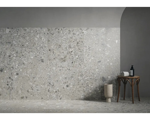 Modern gestalteter Raum mit Wand- und Bodenfliesen in Terrazzo-Optik, einem runden Beistelltisch aus Holz und einer Bodenvase.