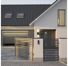 Moderner Hauseingang mit grauem Lamellenzaun, weißer Fassade, dunklem Ziegeldach und Garage mit Sektionaltor.