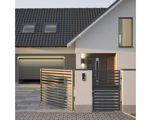 Moderner Hauseingang mit grauem Lamellenzaun, weißer Fassade, dunklem Ziegeldach und Garage mit Sektionaltor.