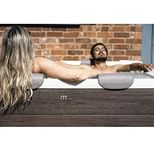 Ein Mann und eine Frau entspannen in einem MSpa Whirlpool mit Außenverkleidung in Holzoptik vor einer Ziegelwand.