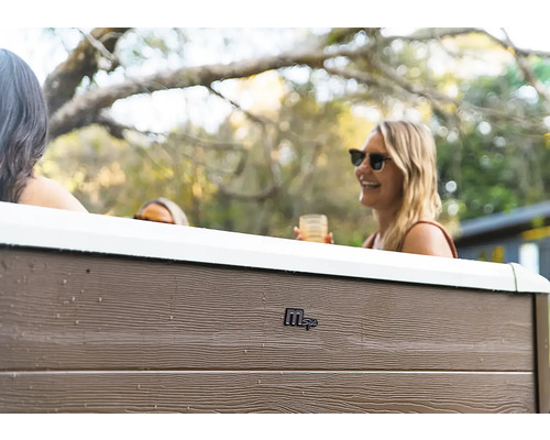 Außenansicht eines MSpa Whirlpools mit Paneelen in Holzoptik und Personen im Garten.