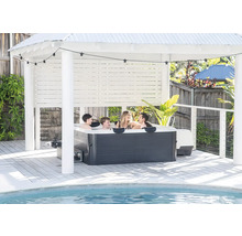 Familie im Whirlpool unter hellem Pavillon auf Holzterrasse am Pool mit Lichterkette.