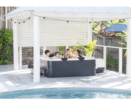 Familie im Whirlpool unter hellem Pavillon auf Holzterrasse am Pool mit Lichterkette.