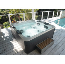 Außenwhirlpool mit dunkelgrauer Verkleidung und weißer Innenschale, Nackenkissen und sprudelndem Wasser auf einer Holzterrasse.