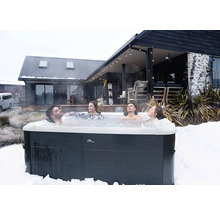 Vier Personen entspannen in einem MSpa Whirlpool im Freien inmitten einer Schneelandschaft vor einem modernen Holzhaus.