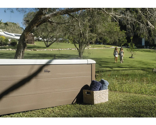 MSpa Whirlpool im weitläufigen Garten auf Rasen, Außenverkleidung in Holzoptik, Flechtkorb mit Handtüchern, helle und großzügige Atmosphäre.