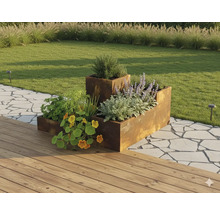 Modulares Hochbeet aus Cortenstahl in einem Garten mit Pflanzen, neben einer Holzterrasse und einem Steinweg.