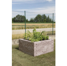 Hochbeet aus Steinblöcken im Garten, bepflanzt mit Kräutern und Pflanzen vor einem Zaun.