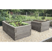 L-förmiges Hochbeet aus strukturierten Blöcken mit Bepflanzung auf einer Kiesfläche im Garten.