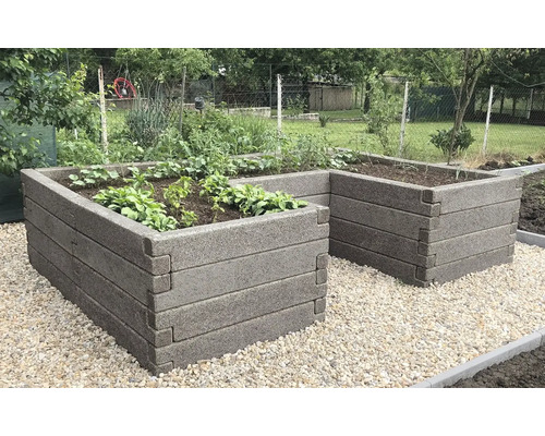 L-förmiges Hochbeet aus strukturierten Blöcken mit Bepflanzung auf einer Kiesfläche im Garten.
