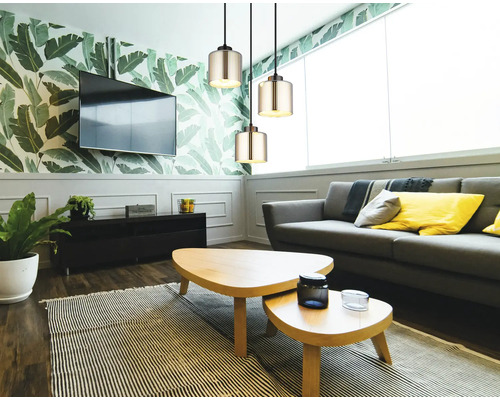 Modernes Wohnzimmer mit drei zylindrischen Glas-Pendelleuchten, grauem Sofa, Holz-Couchtischen und botanischer Tapete.