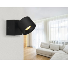 Moderner schwarzer verstellbarer Wandstrahler in einem hellen, geräumigen Wohnzimmer mit weißem Sofa und transparenten Vorhängen.